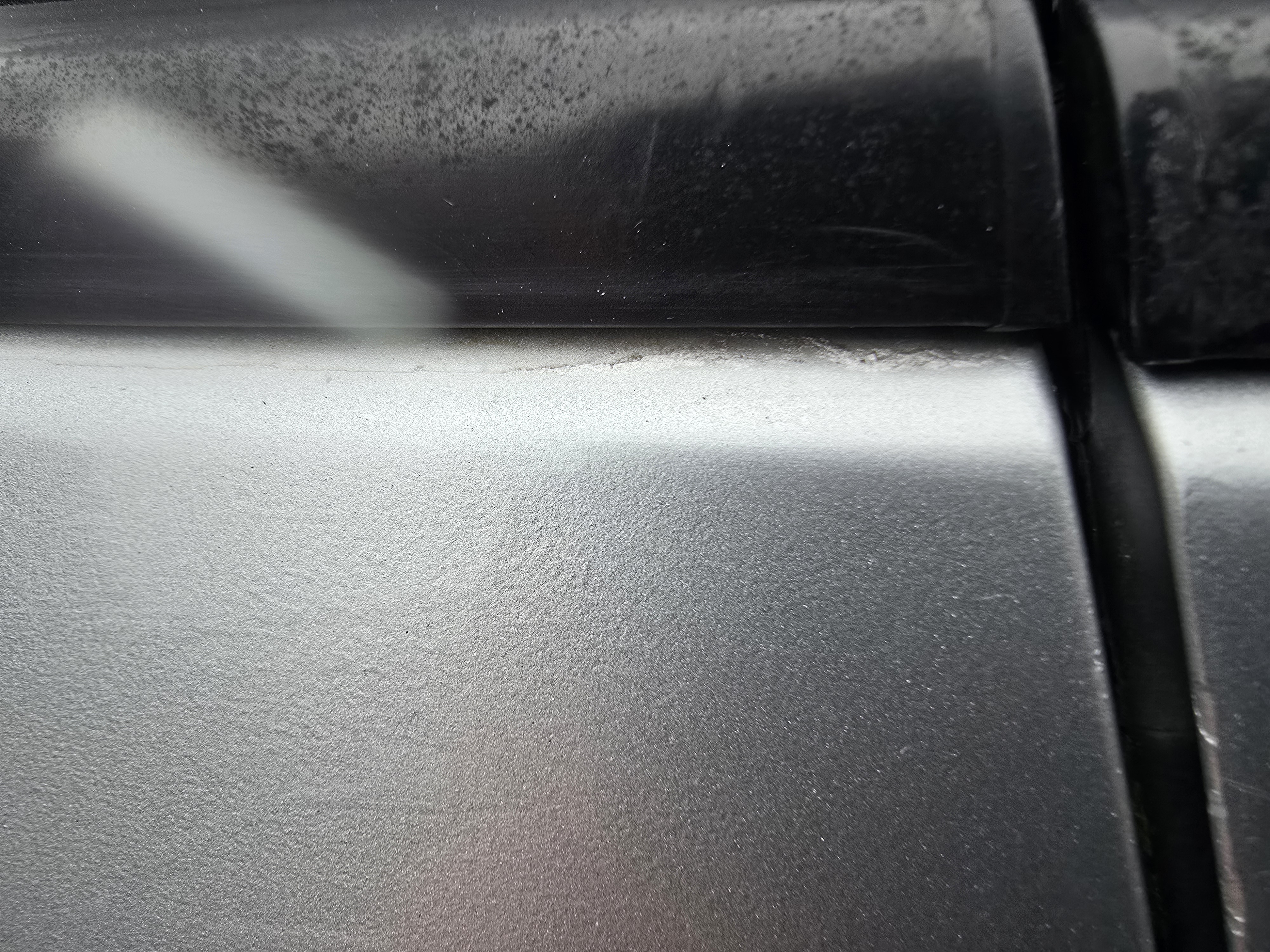 Close-up of lacquer lifting along the top edge of a previously repainted silver door, showing poor adhesion from an earlier repair.