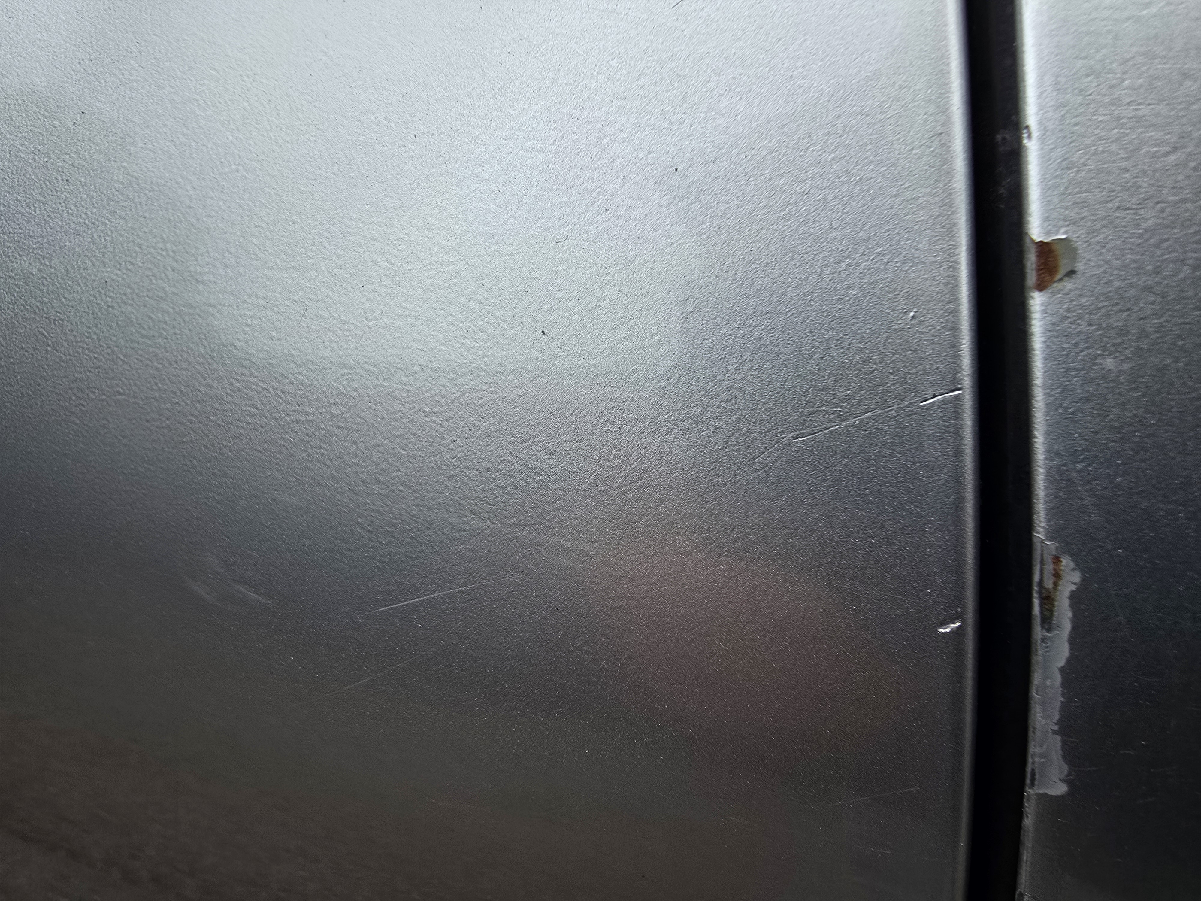 Close-up of a previously repaired silver panel showing faint sanding marks visible beneath the clear coat, indicating poor paint preparation before refinishing.